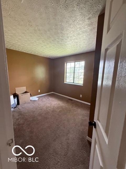 spare room featuring carpet flooring, a textured ceiling, and baseboards