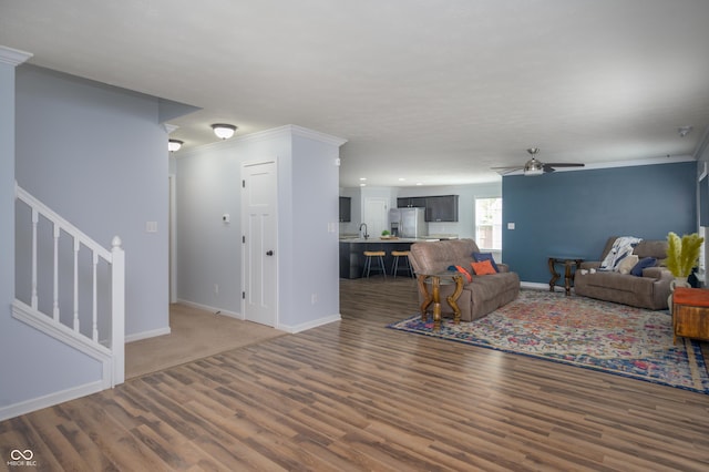 living area featuring stairs, a ceiling fan, baseboards, wood finished floors, and ornamental molding