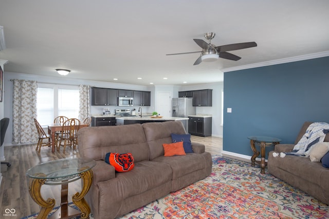 living room with crown molding, light wood-style flooring, a ceiling fan, baseboards, and recessed lighting