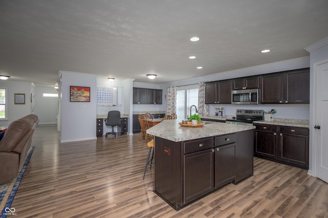 kitchen with dark brown cabinetry, open floor plan, ornamental molding, a breakfast bar, and stainless steel appliances