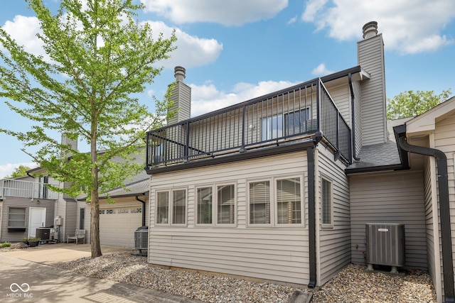 1030 Stratford Hall Unit 17-3, Indianapolis, IN 46260 - back of property with a balcony, central AC unit, concrete driveway, a chimney, and a garage