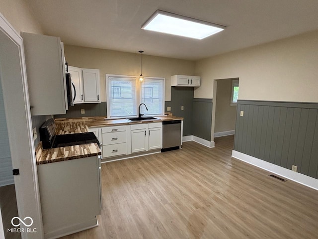 kitchen with a sink, a wainscoted wall, light wood-style floors, wood counters, and stainless steel appliances
