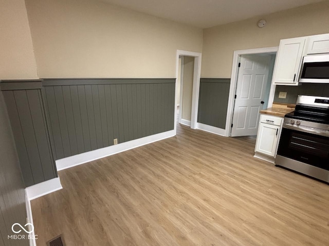kitchen featuring visible vents, white cabinetry, appliances with stainless steel finishes, and wainscoting