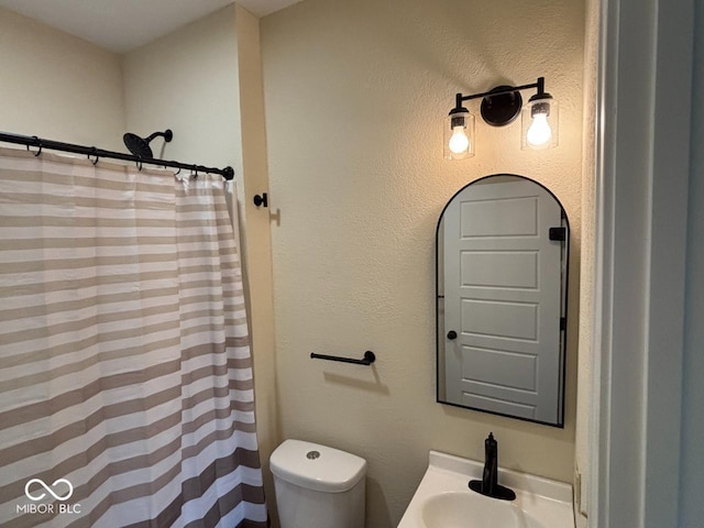 full bath featuring a shower with shower curtain, toilet, and a sink