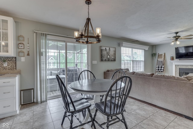 dining space with light tile patterned floors, ceiling fan with notable chandelier, and a glass covered fireplace