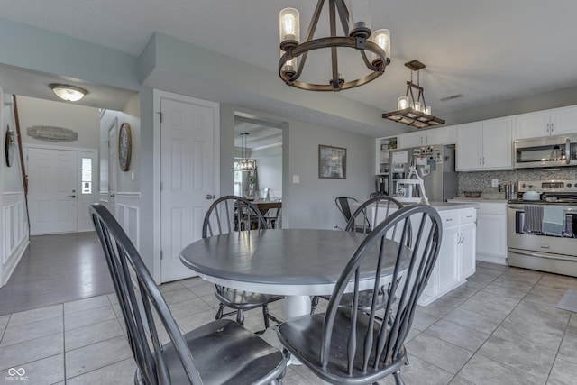 dining space with visible vents, a decorative wall, a wainscoted wall, a chandelier, and light tile patterned floors