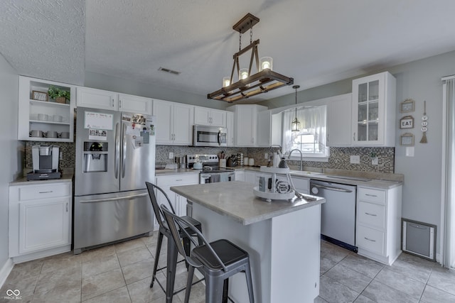 kitchen with visible vents, white cabinetry, a sink, appliances with stainless steel finishes, and backsplash