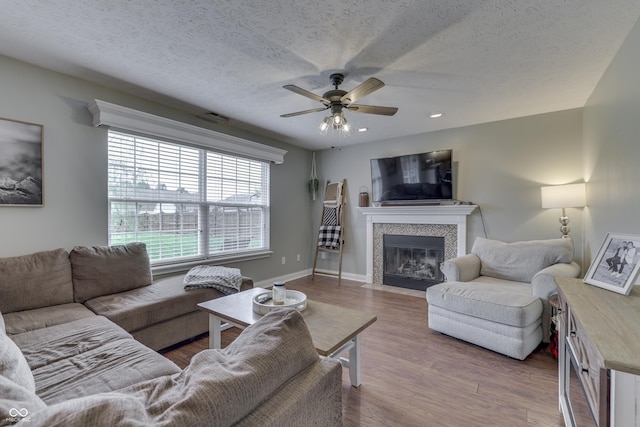 living room with a textured ceiling, ceiling fan, wood finished floors, and a fireplace