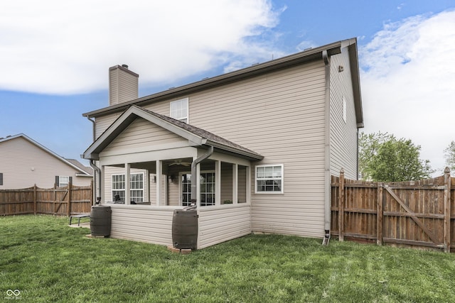 back of house featuring a lawn, a chimney, a fenced backyard, and a sunroom