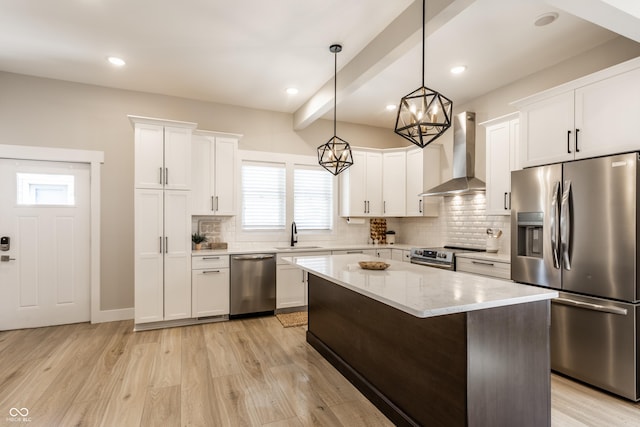 kitchen with wall chimney range hood, a sink, light wood-style floors, stainless steel appliances, and tasteful backsplash