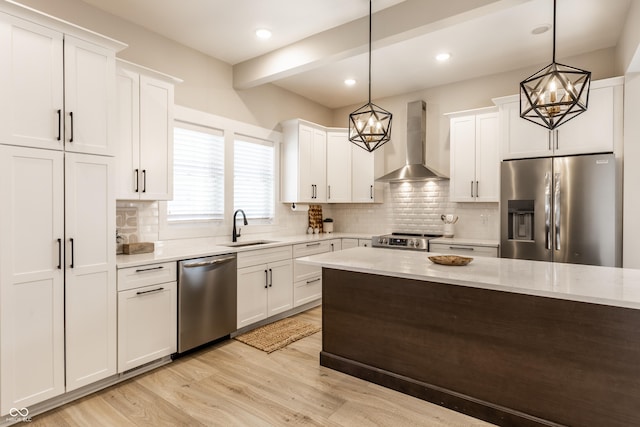 kitchen featuring wall chimney range hood, stainless steel appliances, a chandelier, and a sink