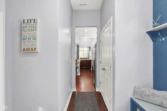 hallway featuring dark wood finished floors, baseboards, and arched walkways
