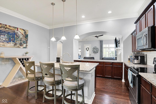kitchen featuring stainless steel appliances, dark wood-type flooring, arched walkways, a center island with sink, and ornamental molding