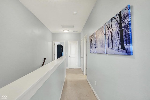 corridor featuring light carpet, baseboards, and an upstairs landing