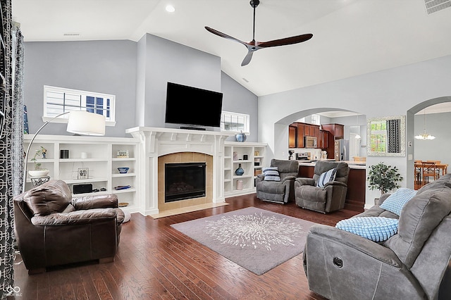 living area with arched walkways, a ceiling fan, dark wood-style floors, a fireplace, and high vaulted ceiling