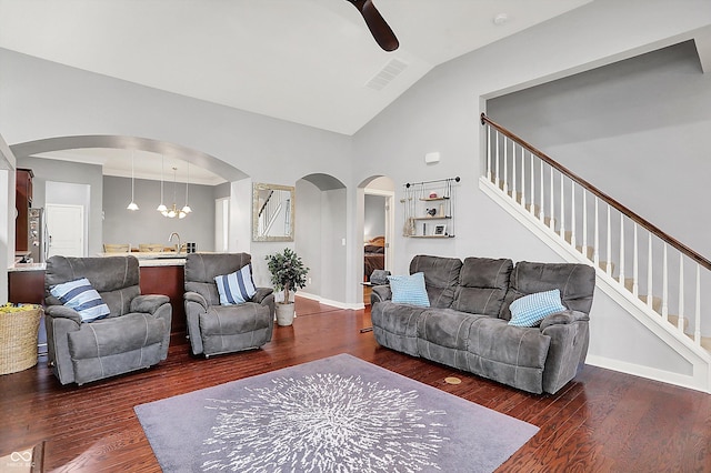 living area with arched walkways, stairs, dark wood-type flooring, and vaulted ceiling