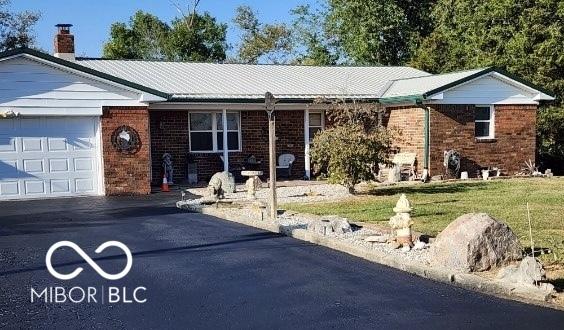 single story home with a chimney, a front yard, a garage, brick siding, and aphalt driveway