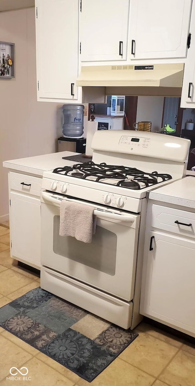 kitchen with light countertops, white gas stove, light tile patterned flooring, and white cabinetry