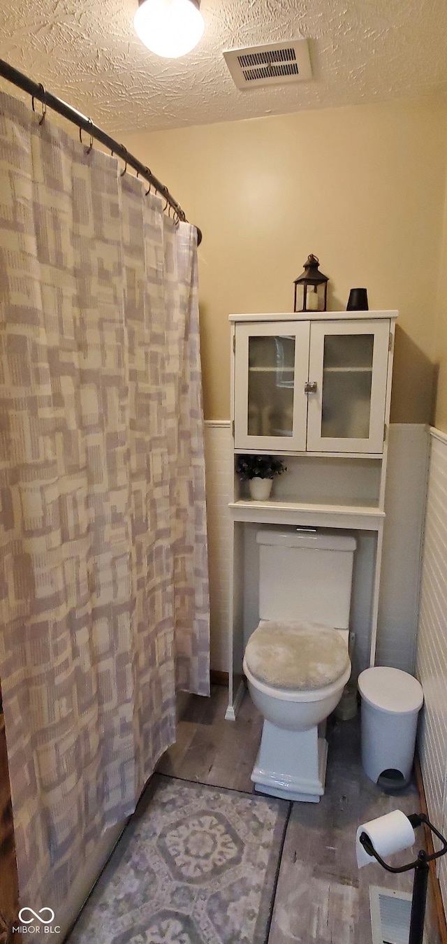 bathroom with wainscoting, toilet, a textured ceiling, and visible vents