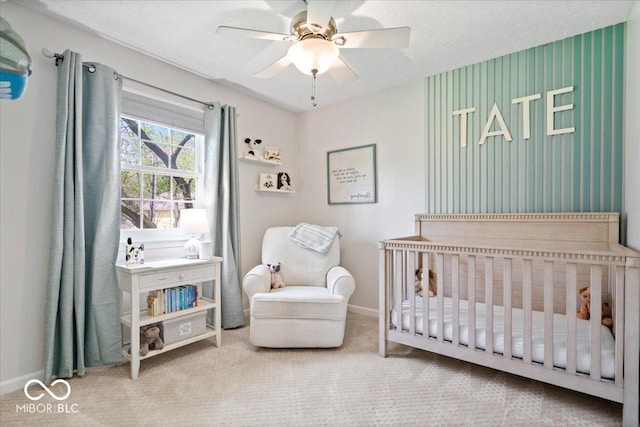 carpeted bedroom featuring baseboards, a ceiling fan, a crib, and a textured ceiling