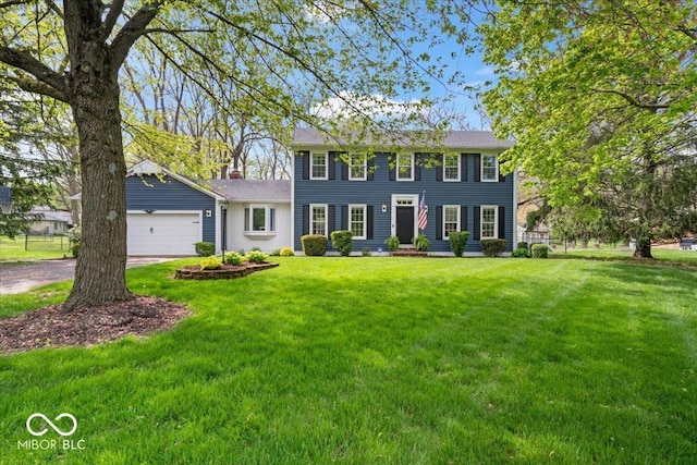 colonial inspired home with an attached garage, a front lawn, driveway, and a chimney