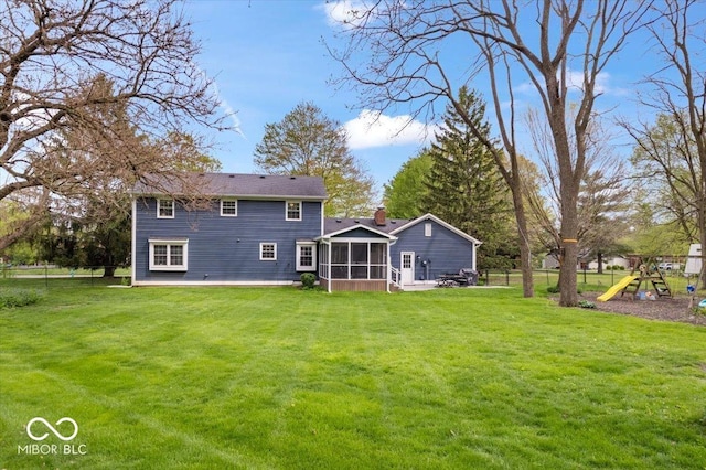 back of house featuring a sunroom, a playground, a lawn, and fence