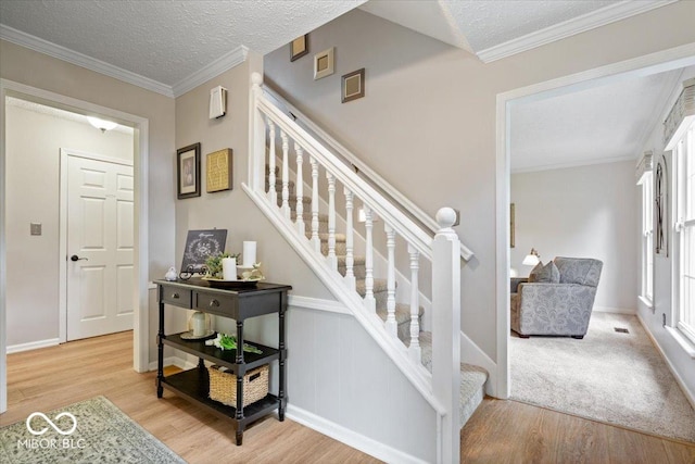 stairway with baseboards, ornamental molding, a textured ceiling, and wood finished floors