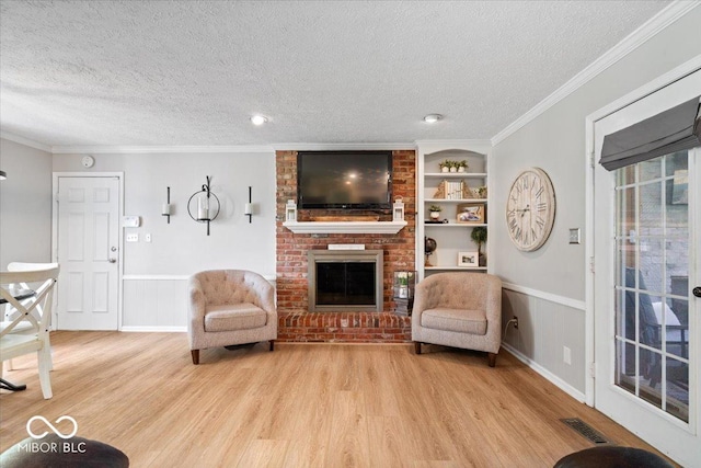 living room featuring a fireplace, a textured ceiling, built in shelves, light wood-type flooring, and visible vents