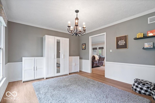 unfurnished dining area with an inviting chandelier, a textured ceiling, french doors, wood finished floors, and ornamental molding