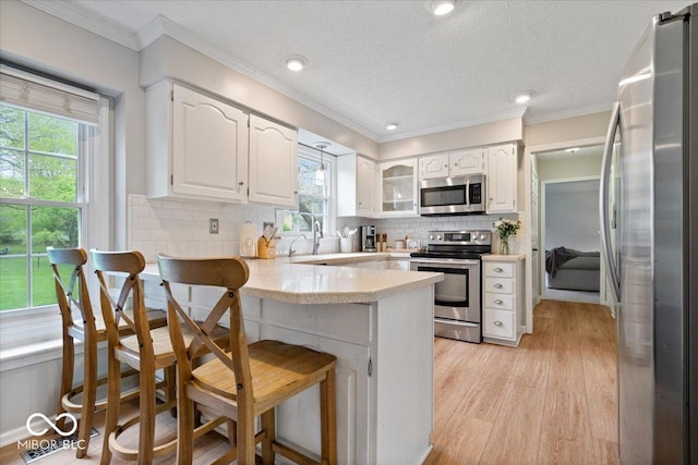 kitchen with decorative backsplash, a peninsula, light countertops, white cabinets, and stainless steel appliances