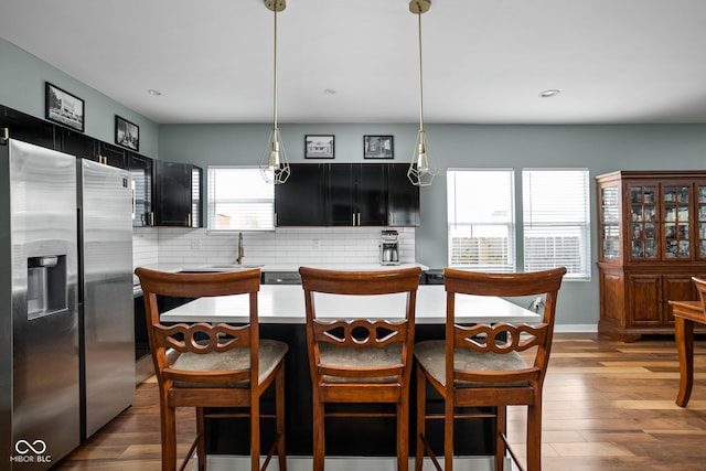 kitchen featuring dark cabinets, stainless steel fridge with ice dispenser, tasteful backsplash, and light countertops