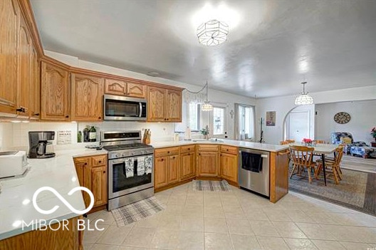 1391 S River Rd, Covington, IN 47932 - kitchen with appliances with stainless steel finishes, a sink, light countertops, brown cabinetry, and a peninsula