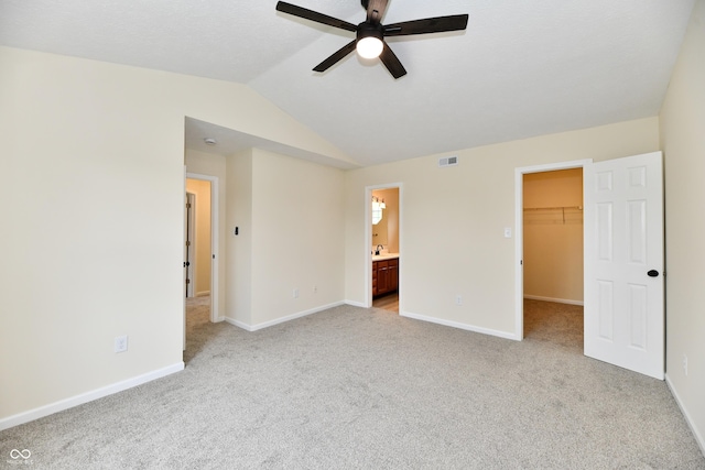 unfurnished bedroom featuring a walk in closet, baseboards, light carpet, and lofted ceiling