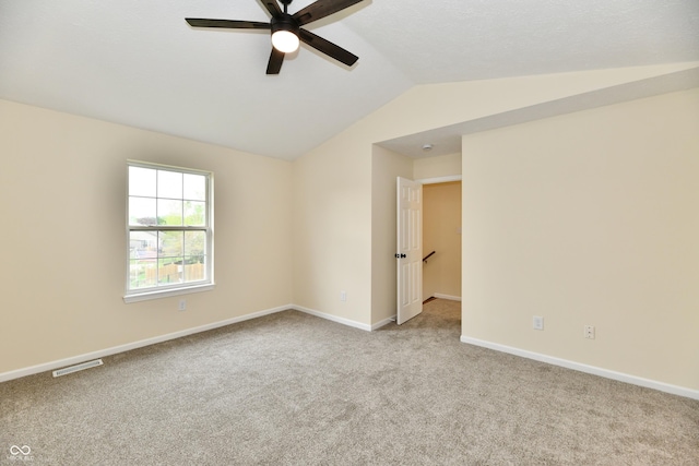 carpeted spare room with baseboards, ceiling fan, vaulted ceiling, and visible vents