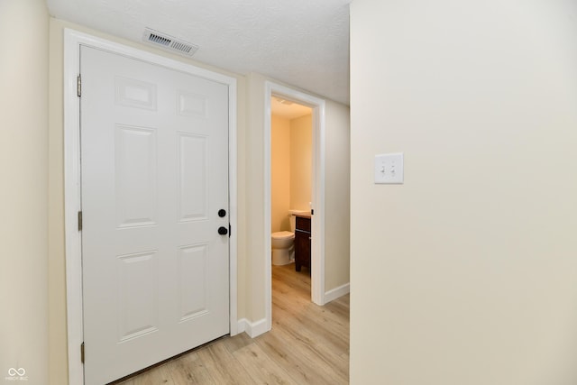 hallway with visible vents, a textured ceiling, baseboards, and light wood-type flooring