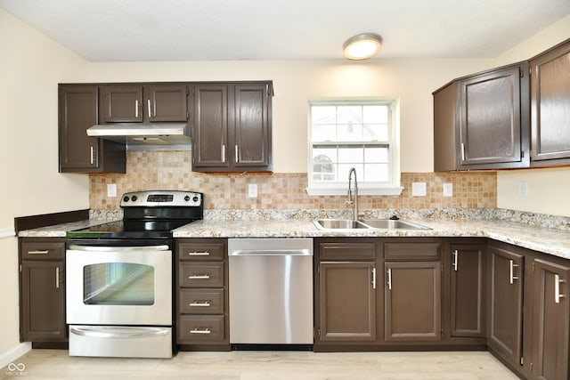 kitchen with appliances with stainless steel finishes, tasteful backsplash, a sink, light wood-type flooring, and under cabinet range hood