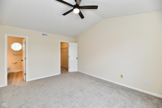 unfurnished bedroom featuring carpet flooring, a walk in closet, baseboards, vaulted ceiling, and visible vents