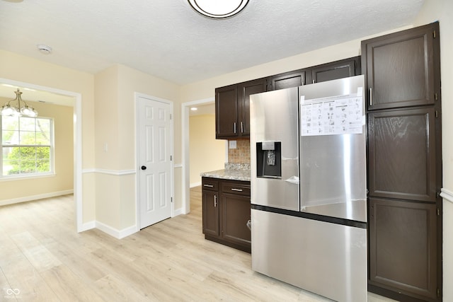 kitchen with dark brown cabinetry, stainless steel fridge, tasteful backsplash, light wood finished floors, and a notable chandelier