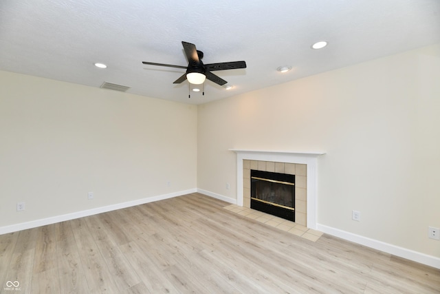 unfurnished living room featuring light wood-style floors, ceiling fan, visible vents, and a tile fireplace