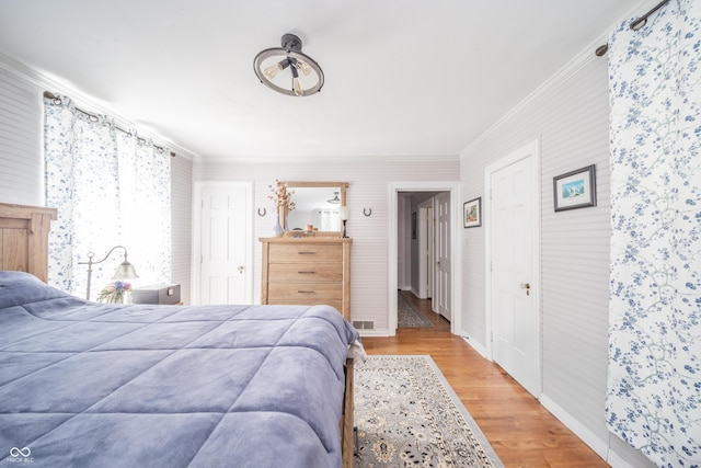 bedroom with baseboards, ornamental molding, light wood finished floors, and visible vents