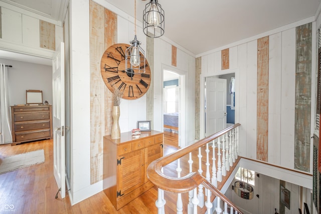 hallway featuring ornamental molding, light wood finished floors, and wood walls