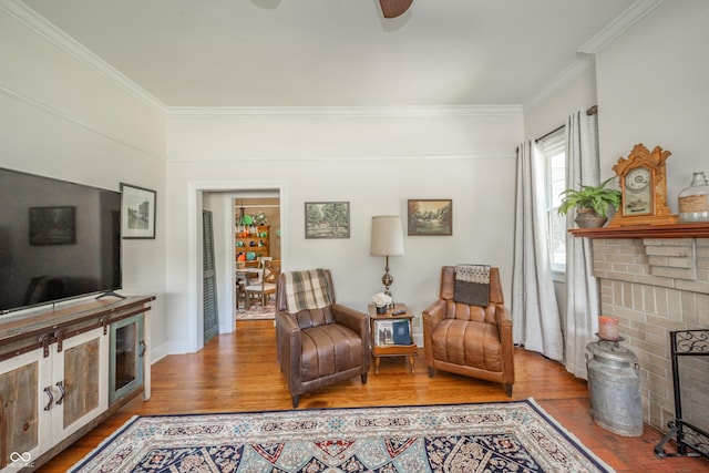 sitting room featuring ceiling fan, crown molding, a brick fireplace, wood finished floors, and baseboards