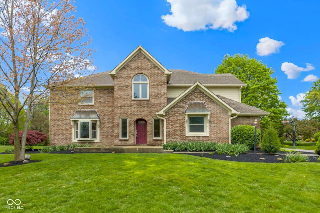 view of front of home featuring brick siding, a shingled roof, and a front lawn