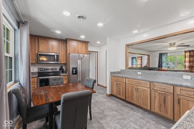 kitchen with brown cabinets, light stone counters, ceiling fan, and appliances with stainless steel finishes