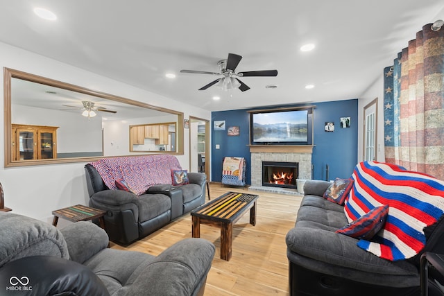 living room featuring a stone fireplace, light wood-style floors, ceiling fan, and recessed lighting