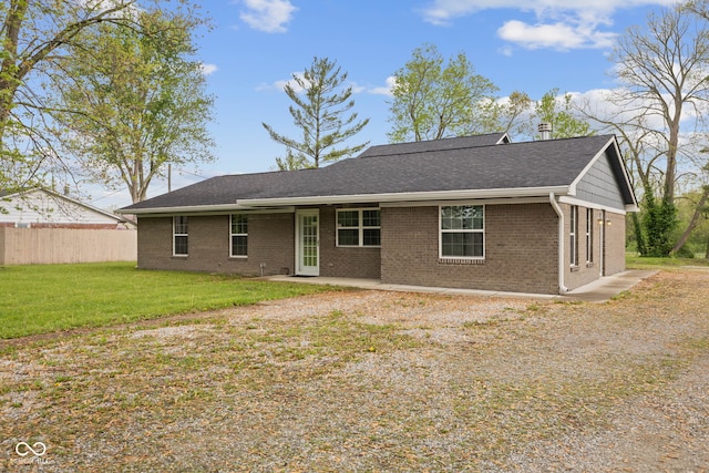 back of house featuring fence, a shingled roof, brick siding, and a lawn