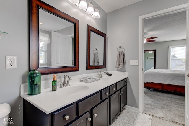 ensuite bathroom with double vanity, a ceiling fan, tile patterned flooring, and baseboards