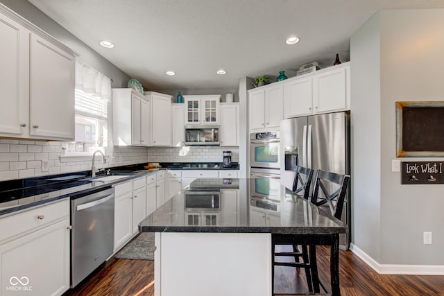 kitchen with stainless steel appliances, a sink, dark wood-style floors, a center island, and a kitchen bar