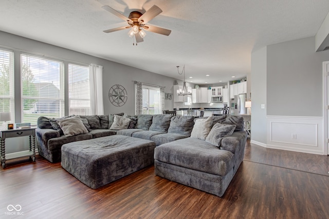 living room featuring a ceiling fan, dark wood-style floors, a chandelier, and wainscoting