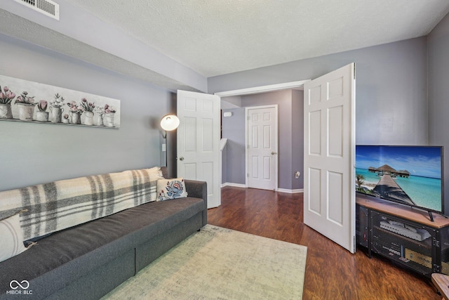 living room featuring visible vents, a textured ceiling, baseboards, and wood finished floors